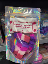 Load image into Gallery viewer, A clear gift bag filled with colourful, four-toned handmade Raspberry Creme rainbow bath rocks with a decorative product label.

